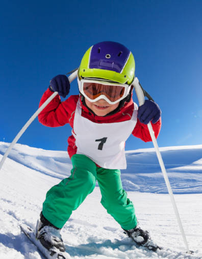 Cute little skier posing with poles at sunny day